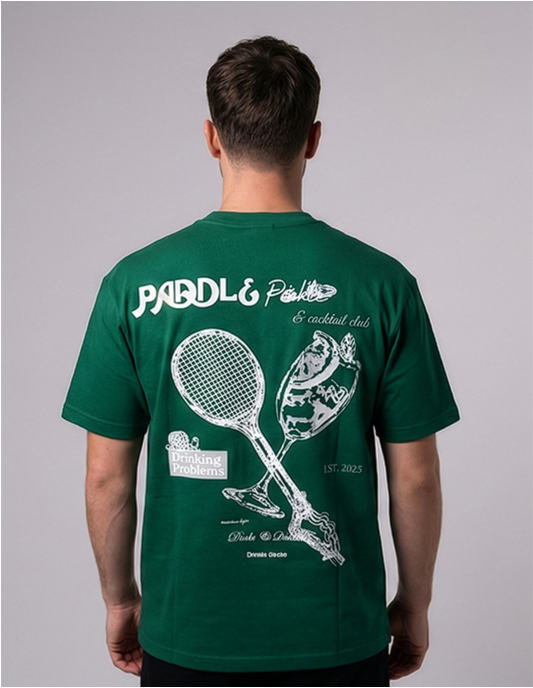Person wearing a green t-shirt with paddle and racket design on the back against a gray background