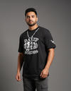 Man wearing a black t-shirt with white text and graphics on a gray background