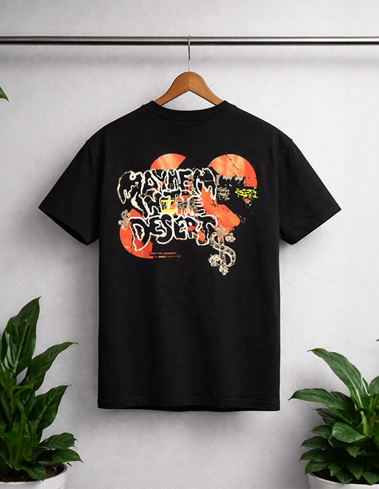Black t-shirt with graphic design on a hanger against a white wall with plants.